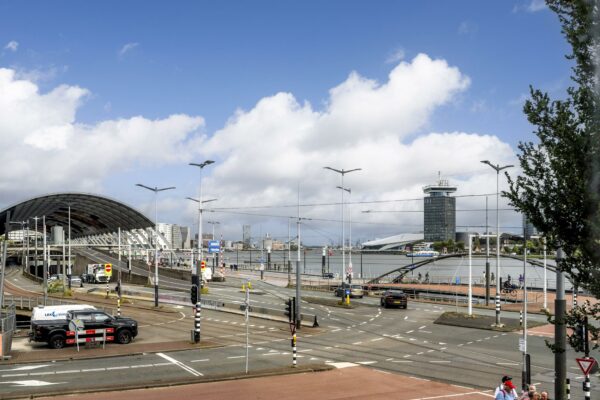 Uitzicht op de De Ruijterkade in Amsterdam met het stationsoverkapping, het IJ en de A'DAM Toren op de achtergrond.